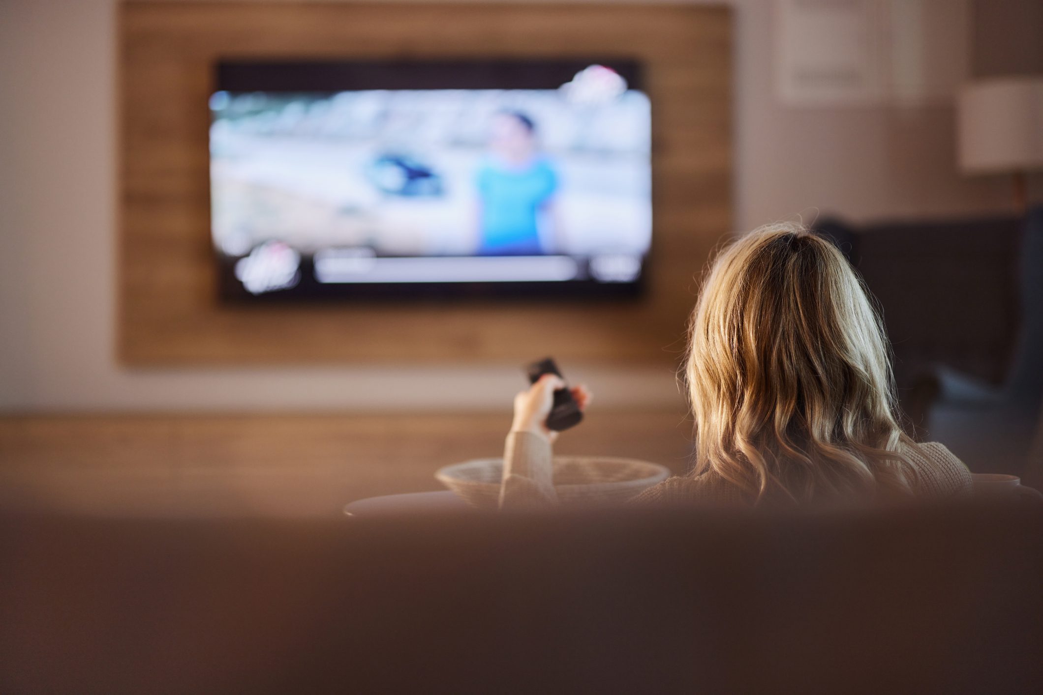 Back view of relaxed woman watching TV at home.